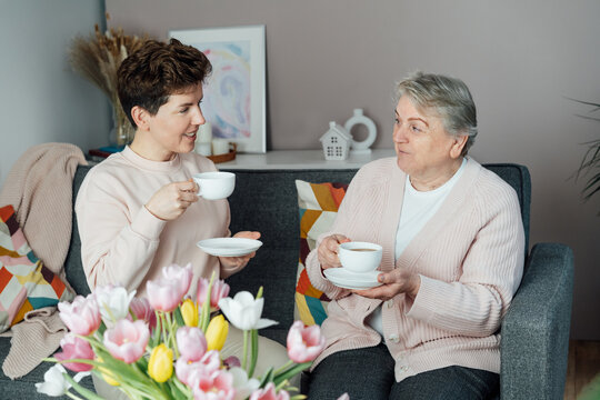 Young woman and her senior mom or grandma enjoy tea and conversation, sharing tender moment together. Parenting love, care and generations unity. Happy family enjoying weekend together at care home.