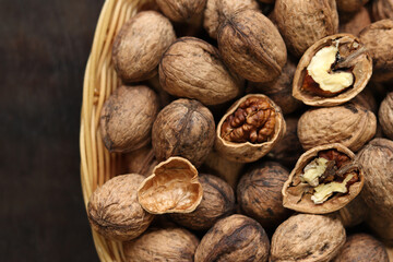 Walnuts in a wicker basket on a dark wooden background. Nuts in an oval basket, top view. Heap of walnuts in shells, close-up, background. Healthy eating. Harvest, agriculture
