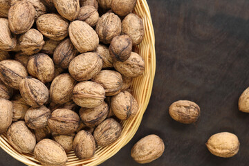 Walnuts in a wicker basket on a dark wooden background. Nuts in an oval basket, top view. Heap of walnuts in shells, close-up, background. Healthy eating. Harvest, agriculture
