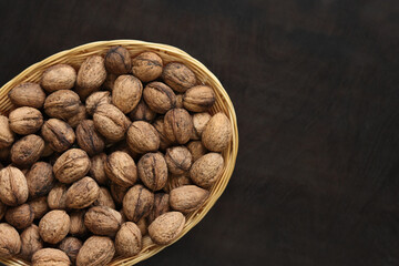Walnuts in a wicker basket on a dark wooden background. Nuts in an oval basket, top view. Heap of walnuts in shells, close-up, background. Healthy eating. Harvest, agriculture
