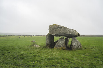 Carreg Samson, a prehistoric dolmen with a large capstone supported by upright stones, surrounded by lush grass and mist, evoking a serene, mystical atmosphere in a tranquil landscape.