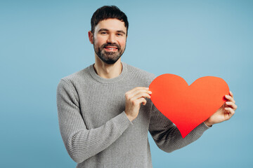 Smiling man holding a big red heart on blue background