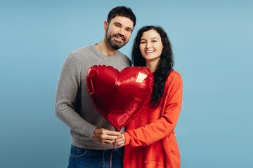 Happy couple holding red heart shaped balloon on blue background