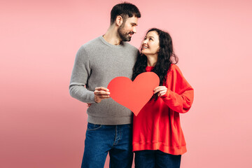Happy couple, attractive woman and man holding big red heart on pink background