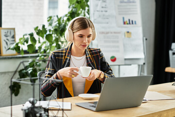 Attractive young woman in a stylish checkered blazer enjoys coffee while working on her laptop.