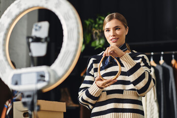 A stylish young woman energetically curates her outfit while recording herself on a smartphone.