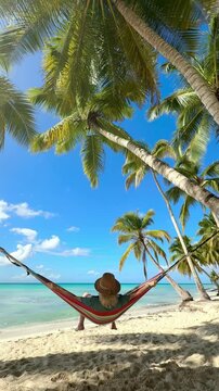 relaxing in vacation, woman on a colorful hammock on a tropical beach with palms and turquoise sea
