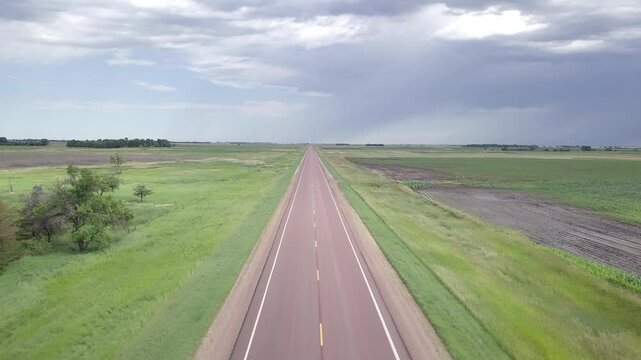 Flying straight down empty road in South Dakota with storm clouds in background.