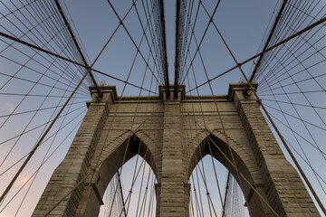 Brooklyn Bridge close up detail looking up at suspension cables at sunrise (beautiful landmark travel tourism destination in NYC) iconic New York City attraction over east river downtown Manhattan USA