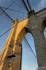 Naklejka premium Brooklyn Bridge close up detail looking up at suspension cables at sunrise (beautiful landmark travel tourism destination in NYC) iconic New York City attraction over east river downtown Manhattan USA