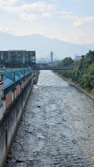 Fototapeta premium Elevated view of a canal, modern building, and distant mountains under a partly cloudy sky.