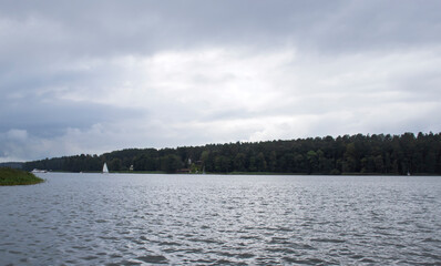 A serene landscape featuring a calm lake surrounded by dense forests under a cloudy sky, creating a peaceful atmosphere for outdoor activities and nature enthusiasts.