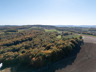 Fototapeta premium Aerial view of a lush green landscape with vibrant autumn colors, showcasing farmland and rolling hills under a clear blue sky.