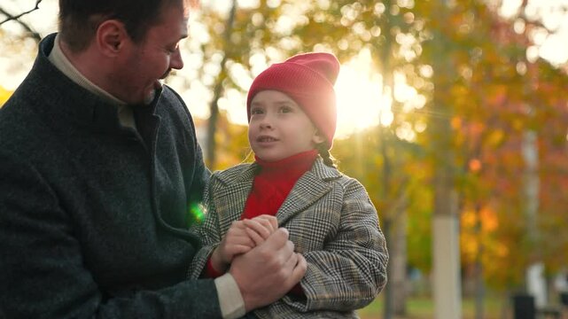 Dad listens attentively to emotional daughter talking about impressions of walk. Dad adjusts hat on head of daughter with care. Positive daughter sits with dad in park sharing plans for next stroll