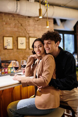 A beautiful young couple celebrates their love at a restaurant, sharing smiles and wine.