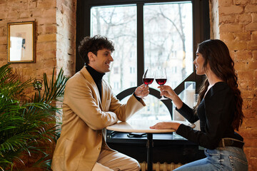 A charming couple shares a romantic toast with glasses of wine in a cozy restaurant setting.