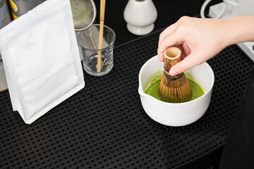 Barista making green tea in to white cup at the coffee shop.Close up hand while preparing matcha menu from green tea powder on black background.