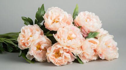 Soft pink peony bouquet elegantly arranged on a light gray backdrop showcasing delicate petals and lush green leaves