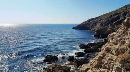 Fototapeta premium Serene coastal view from a mountain overlooking the tranquil sea and rocky shoreline under bright blue skies and gentle waves.