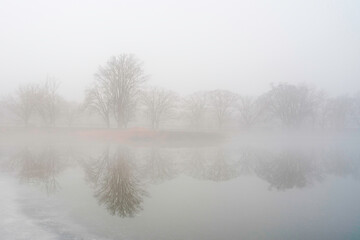 Foggy winter landscape with trees in the mist and snow-covered ice  over the lake in New Haven, Connecticut, USA