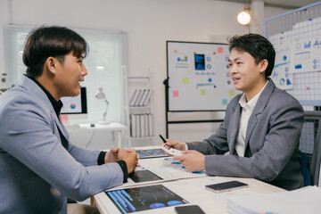 Two asian business people discussing and working together with financial charts and digital tablet at modern office, analyzing financial data and company's performance