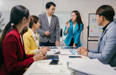 Asian businesspeople analyzing charts and graphs, collaborating on project strategy during a...