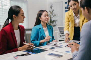 Four asian businesswomen are having a meeting in a modern office, analyzing financial charts and discussing business strategies, collaborating on a project