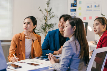 Four asian businesspeople are sitting around a table in a modern office, listening to a presentation and participating in a collaborative discussion