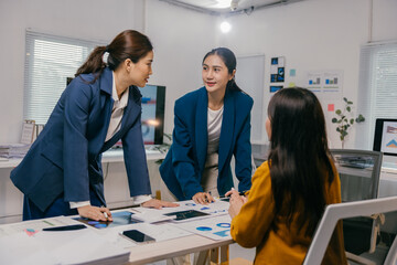 Three asian businesswomen are having a productive meeting in a modern office, analyzing charts and documents spread out on a table, engaging in collaborative discussion and strategic planning