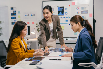 Three asian businesswomen are having a productive meeting in a modern office, analyzing charts, graphs, and financial data, working together to achieve business goals