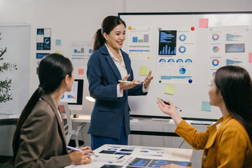 Asian businesswoman leads a meeting with two colleagues, presenting charts and statistics on a...