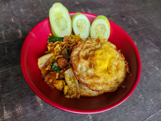 Mie Goreng Close Up, Fried Instant Noodles with Sunny Side Up Egg and Vegetables on Top. Popular...