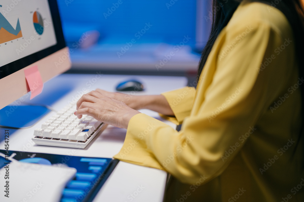 Poster businesswoman wearing yellow jacket is working at night in office typing on keyboard and analyzing f