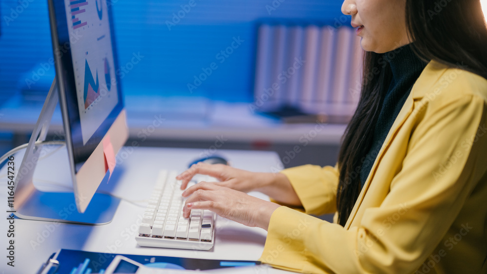 Aufkleber Businesswoman is typing on a white keyboard and working with charts and graphs displayed on a computer screen in a modern office with blue light in the background at night
