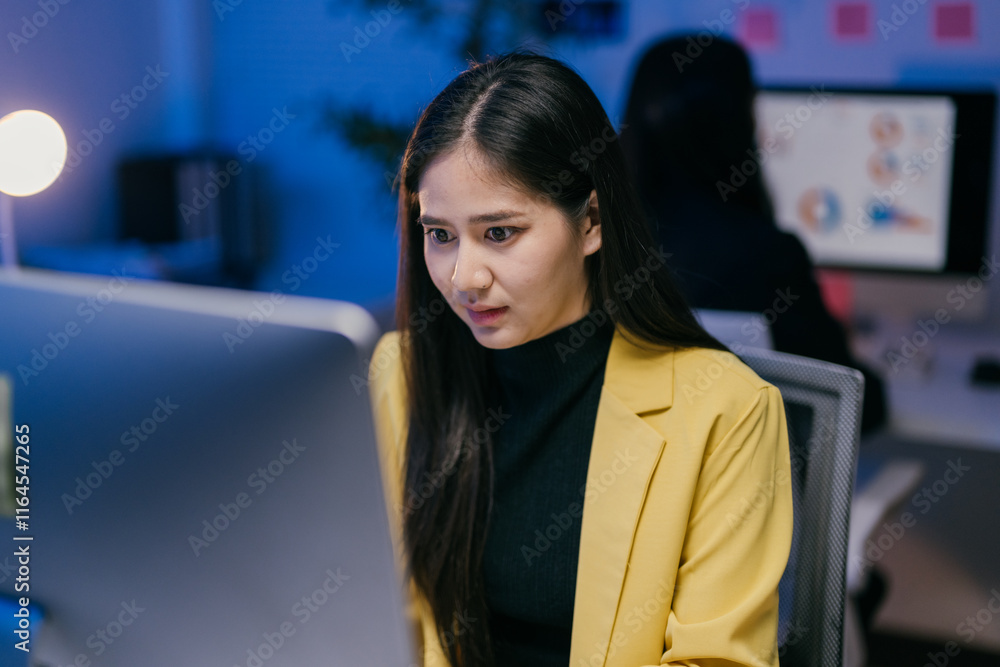 Poster young professional woman concentrating on her tasks on computer screen, working overtime in modern o