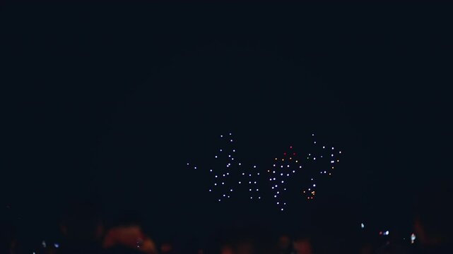 illuminated aerial drone show at glowing night sky, programmed flying robotics light performance over city, people watching and filming, advanced technology concept