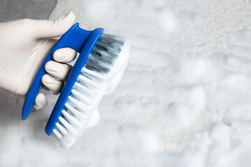 Blue brush on the floor and much foam with hand in rubber glove. Cleaning.