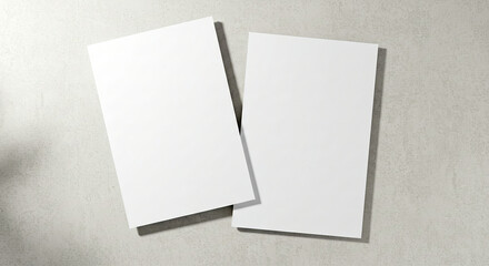 Two empty white rectangle poster mockups lying diagonally on top of each other with soft shadows on neutral light grey concrete background. Flat lay, top view