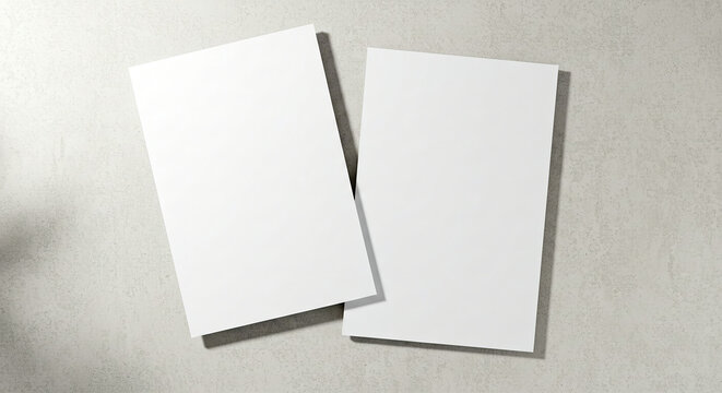Two empty white rectangle poster mockups lying diagonally on top of each other with soft shadows on neutral light grey concrete background. Flat lay, top view