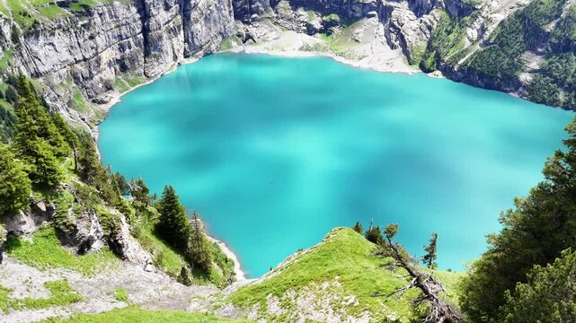 Slow drone flight above grassy cliffs high above the Oeschinensee lake in the  Swiss Alps. Down view towards the turquoise blue lake. Beautiful Swiss mountains, amazing nature. Outdoor adventure, heal
