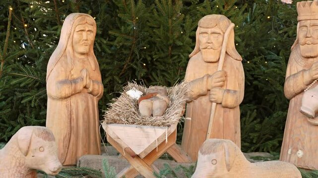 A handcrafted nativity scene features wooden figures of Mary, Joseph, and baby Jesus in a manger, evoking Christmas traditions and religious symbolism, set against a tree-lined background.