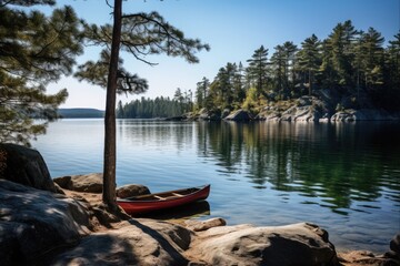 Fototapeta premium Tranquil Blue Waters- Calm Lake with Rocky Shoreline, Pine Trees and Red Canoe for Paddle Adventure