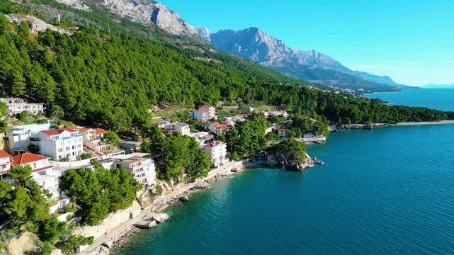 A stunning aerial view of Brela, Croatia, showcasing the iconic Kamen Brela rock formation surrounded by crystal-clear turquoise waters. The coastline is dotted with pristine beaches