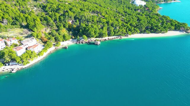 A stunning aerial view of Brela, Croatia, showcasing the iconic Kamen Brela rock formation surrounded by crystal-clear turquoise waters. The coastline is dotted with pristine beaches