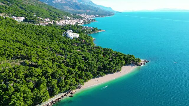 A stunning aerial view of Brela, Croatia, showcasing the iconic Kamen Brela rock formation surrounded by crystal-clear turquoise waters. The coastline is dotted with pristine beaches