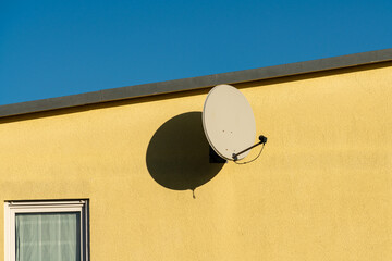 Satellite dish mounted on a vibrant yellow wall in daylight