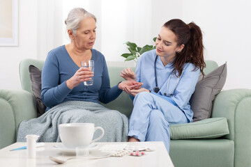 A young, friendly nurse or doctor smiles warmly while helping an elderly woman patient take a pill...