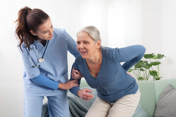 Caring nurse or doctor to take care a senior woman patient while to helps get up from the sofa due to back pain. Nursing at home in medical clinic or in hospice. Concept of healthcare and insurance