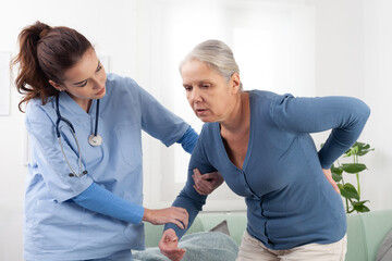 Caring nurse or doctor to take care a senior woman patient while to helps get up from the sofa due to back pain. Nursing at home in medical clinic or in hospice. Concept of healthcare and insurance