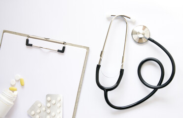 Stethoscope, pills and clipboard on white background